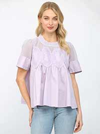 Woman wearing a light purple blouse with lace details on a white background